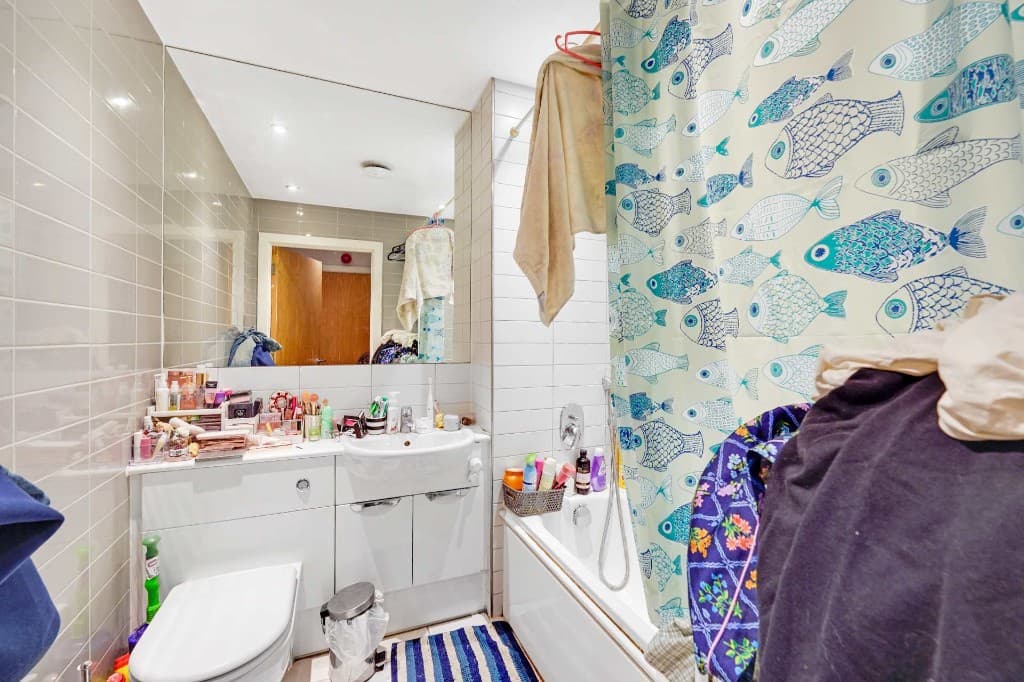 Bathroom cluttered with toiletries, towels and a patterned shower curtain before cleanup