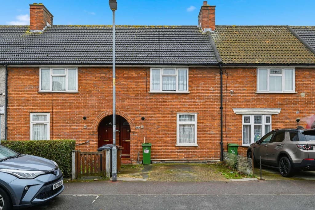 Terraced house exterior with cars parked outside and wheelie bins by the doors